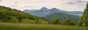 Trachytové kužele Milešovky  a Kletečné při pohledu z vrchů  na pravém břehu Labe.  Jejich vrcholy se tyčí 696 m a 566 m  nad hladinou řeky. Na protější straně  labského údolí zeje rovněž skalní jizva lomu na kamenivo v Dobkovičkách,  pod nímž vede osudná dálnice D8  postižená přirozenými sesuvy,  kterým se zde jen těžko dá zabránit. Foto K. Horáček